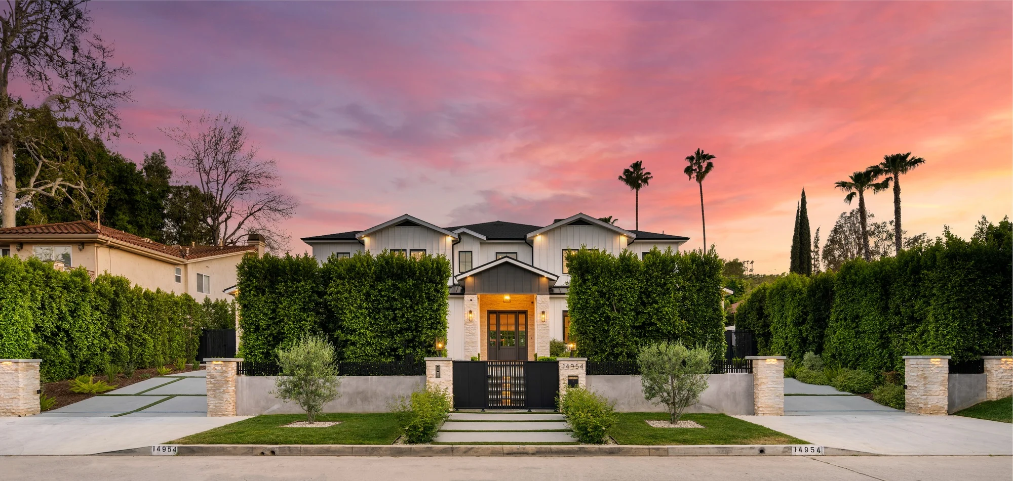 a large house with some bushes around it and a sunset